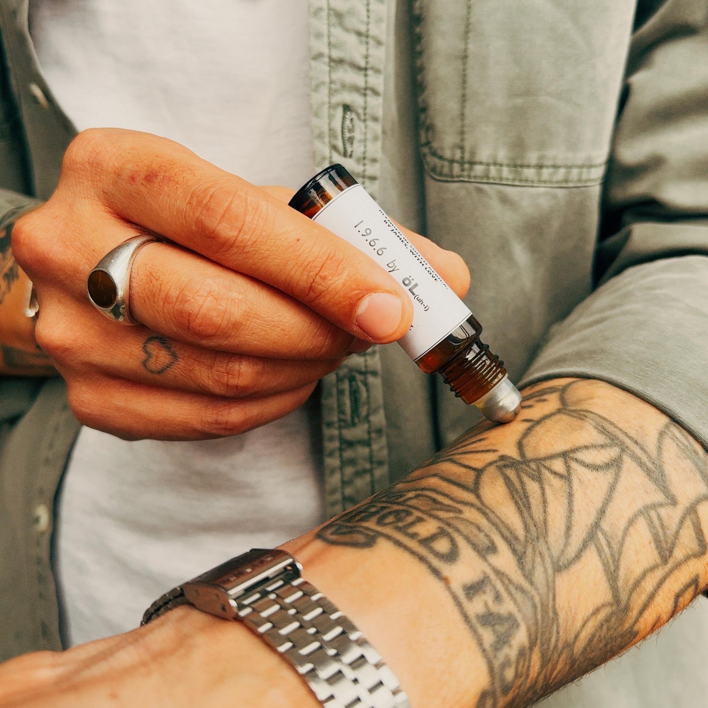 Person holding a small bottle with a dropper on their arm, wearing a watch.